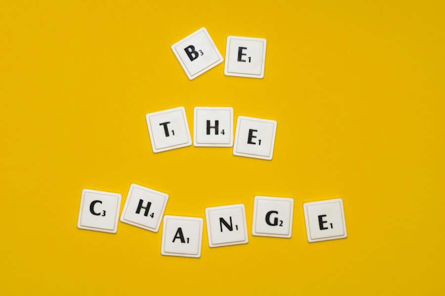 White tiles spelling "Be the Change" arranged in a slight arc on a bright yellow background.